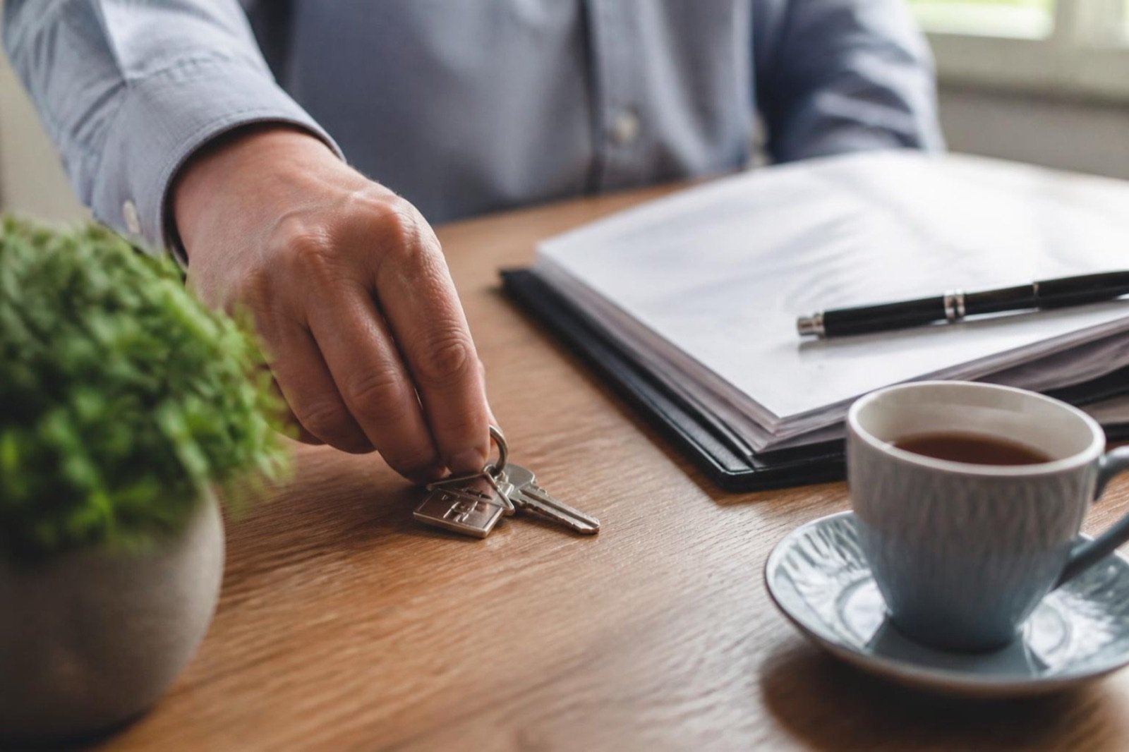 A buyer’s hand picking up a bunch of keys from a folder of papers on a wooden desk